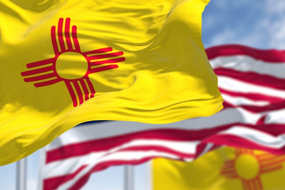 Concept of Rapid Detox in New Mexico. The New Mexico state flag waving along with the national flag of the United States of America. In the background there is a clear sky. New Mexico is a state in the Southwestern United States