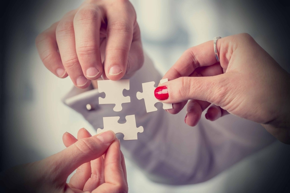 Three hands holding the pieces of a puzzle together