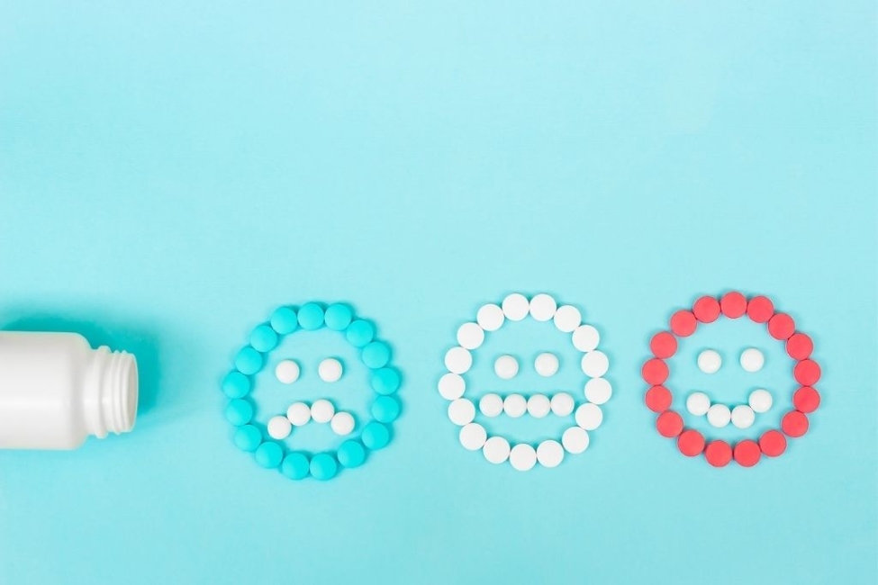 Multicolored pills and funny faces and a plastic bottle on a blue background. The concept of antidepressants and opioids.