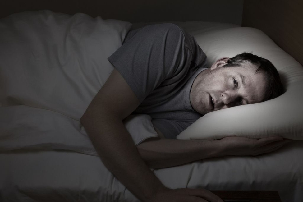 Mature man eyes wide open laying in bed experiencing opiate withdrawal symptoms. Concept of opioid detox without medical supervision.